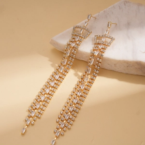 Detailed macro shot of golden crown earrings with long rhinestone tassels on marble