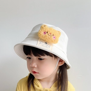 Detail of white cotton bucket hat with plush yellow bear charm and chin strap for kids