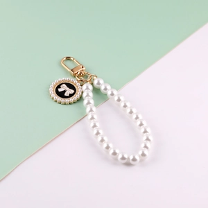 Detail of a pearl wrist strap with a gold clasp and a black bow pendant accessory