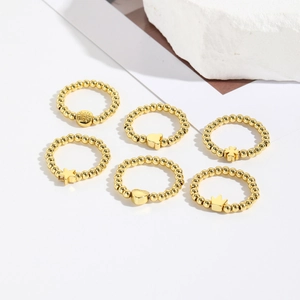 Set of six gold beaded elastic rings with crown and star charms on white background