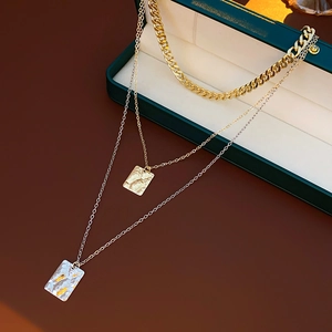 Detail showing multi-layer gold and silver textured square pendants on triple chains