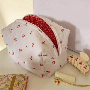 Macro view of white quilted cosmetic bag with red cherry print and checkered lining