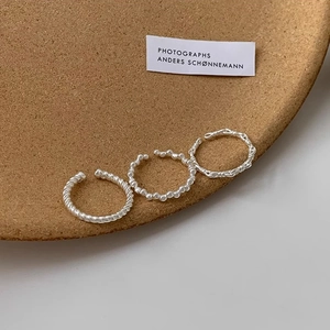 Close-up of three silver textured rings including twisted and beaded bands on a cork tray