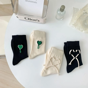 Dettaglio di calzini in cotone con cuori ricamati e lacci con nappe in nero e beige
