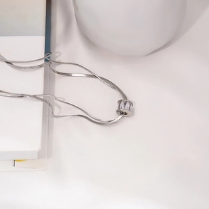 Close-up of silver snake chain necklace with rectangular crystal pendant on white decor