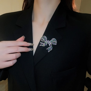 Detailed shot of bow brooch with purple and green zircon on black formal suit