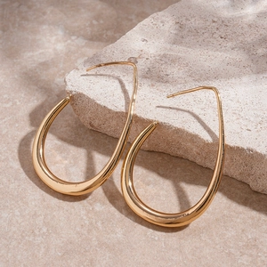 Macro view of gold teardrop earrings placed on natural stone with soft lighting