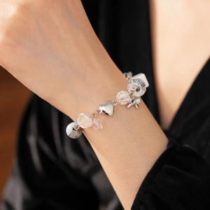 Close-up of beaded bracelet featuring silver star, heart and bow charms on wrist