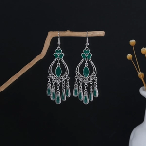 Detail of vintage bohemian dangle earrings with green enamel and silver tassels on wood