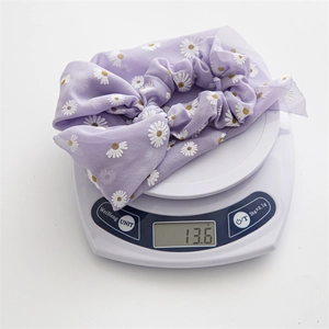 Close-up of lightweight purple chiffon scrunchie with daisy print on a digital scale