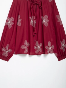 Detail of raspberry red blouse featuring white floral embroidery and lantern sleeve design
