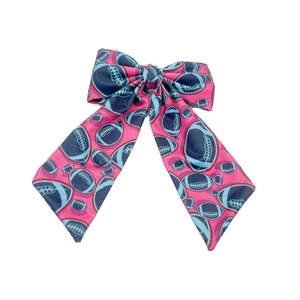 Detailed view of pink fabric hair bow with dark blue football pattern and long ribbon