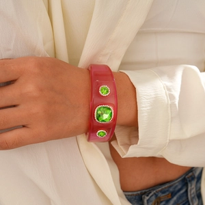 Detailed view of pink resin bangle with green crystal rhinestones on a female wrist
