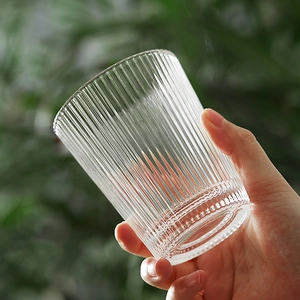 Ins style glass cup with vertical stripes and beaded base held against green plants