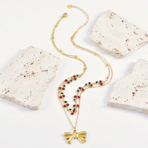 Double-layer gold necklace with red cherry beads and bow pendant on stone props