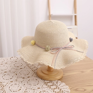 Detailed close-up of straw sun hat featuring wavy openwork edges and pom-pom floral trim