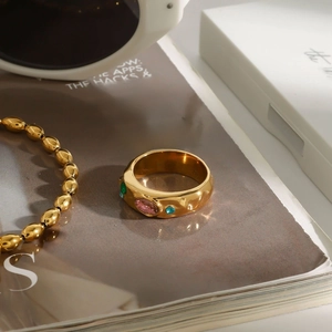Detail of gold hammer-textured ring with pink oval stone and green gems on a magazine