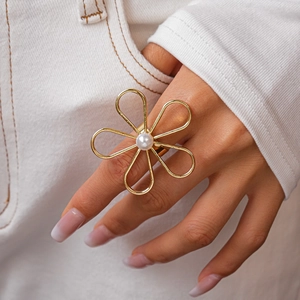 Detailed view of oversized gold floral ring with center pearl worn by a model