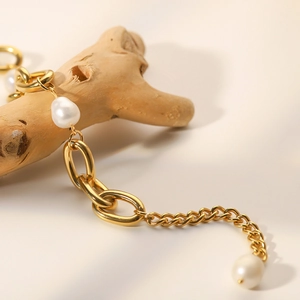 Detail of baroque pearl bracelet with gold link chain on textured wood background