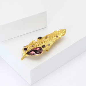 Golden leaf brooch featuring a large pear-shaped purple crystal and small purple rhinestones