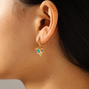 Close-up of golden heart earring with colorful zircon stones on model's ear