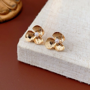 Elegant gold leaf clover stud earrings with center pearl on a textured linen stand