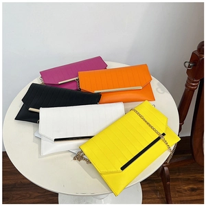 Top view of five colorful PU leather clutch bags with gold chain straps on a white table