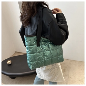 Detail of green quilted tote bag with metallic glossy finish and black strap