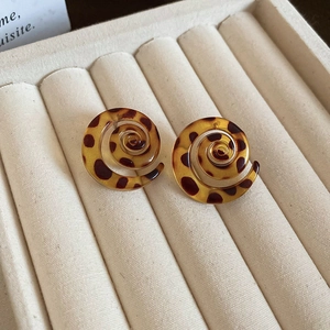 Detailed close-up of leopard print spiral resin earrings on a cream velvet jewelry tray