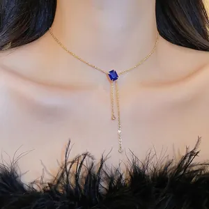Elegant gold necklace with square blue gemstone pendant and asymmetric tassels on model