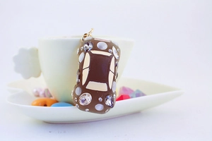 Detail of a brown car-shaped keychain with rhinestones hanging on a beige coffee cup
