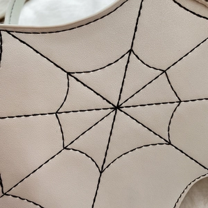 Detailed close-up of spider web embroidery on beige faux leather bag surface