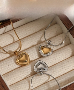 Polished heart pendants in gold and silver finishes displayed on beige velvet lining