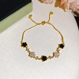 Detail of adjustable gold chain bracelet with black and zircon clover charms
