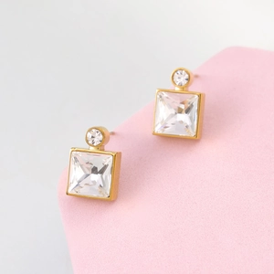 Detail of square princess cut crystal earrings with gold plated base on pink pedestal