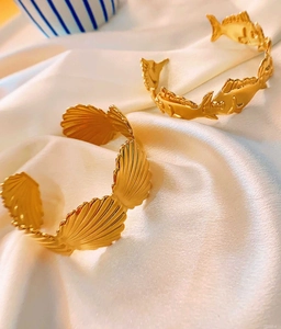 Detailed macro view of two gold open bangles with shell and fish motifs on white silk fabric