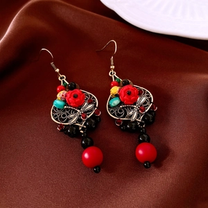 Detailed view of vintage dragonfly earrings with red rose and beads on silk background