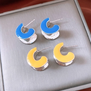 Detailed close-up of blue and yellow C-shaped enamel earrings in a grey jewelry display box