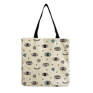 Close-up of canvas tote bag with evil eye and gemstone prints and black nylon handles