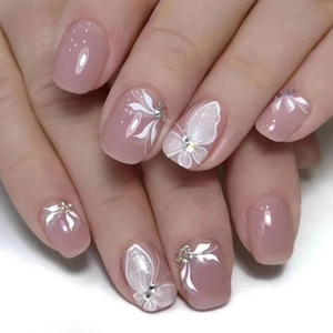 Detail of nude pink press-on nails featuring white floral patterns and silver rhinestones