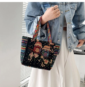 Detail of colorful owl embroidery and floral pattern on black canvas tote with woven handle