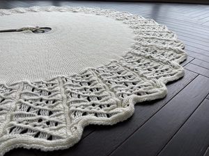 Close-up of cream knitted Christmas tree skirt featuring hollow wave edges and tie detail