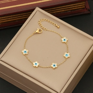 Macro view of gold chain bracelet with white flower charms and blue evil eye details