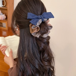 Detail of a dark blue denim bow and plaid scrunchie set on a model's hair in home setting