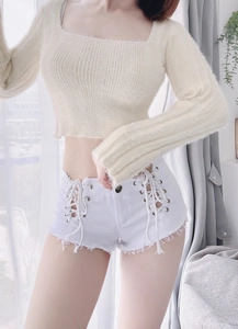 Dettaglio degli shorts in denim bianco con lacci laterali e crop top in maglia beige