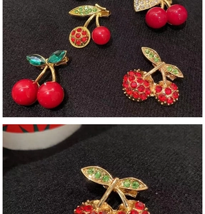Close-up of cherry brooch with red rhinestones and green leaves on black fabric