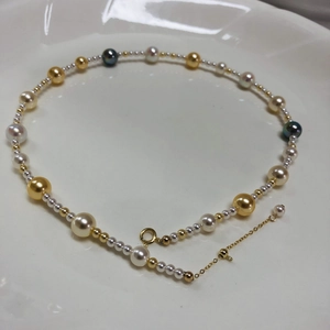 Macro detail of multi-colored pearls and adjustable gold chain on white surface