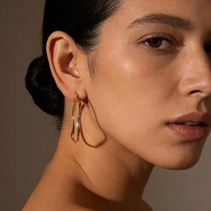 Minimalist geometric twisted gold hoop earrings shown on a model with metallic wavy texture