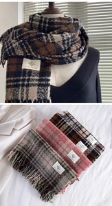 Detail of soft plaid scarf showing thick fringe texture and brand label craftsmanship