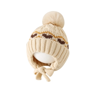 Winter knit baby earflap hat with heart patterns and faux fur pompom in cream white